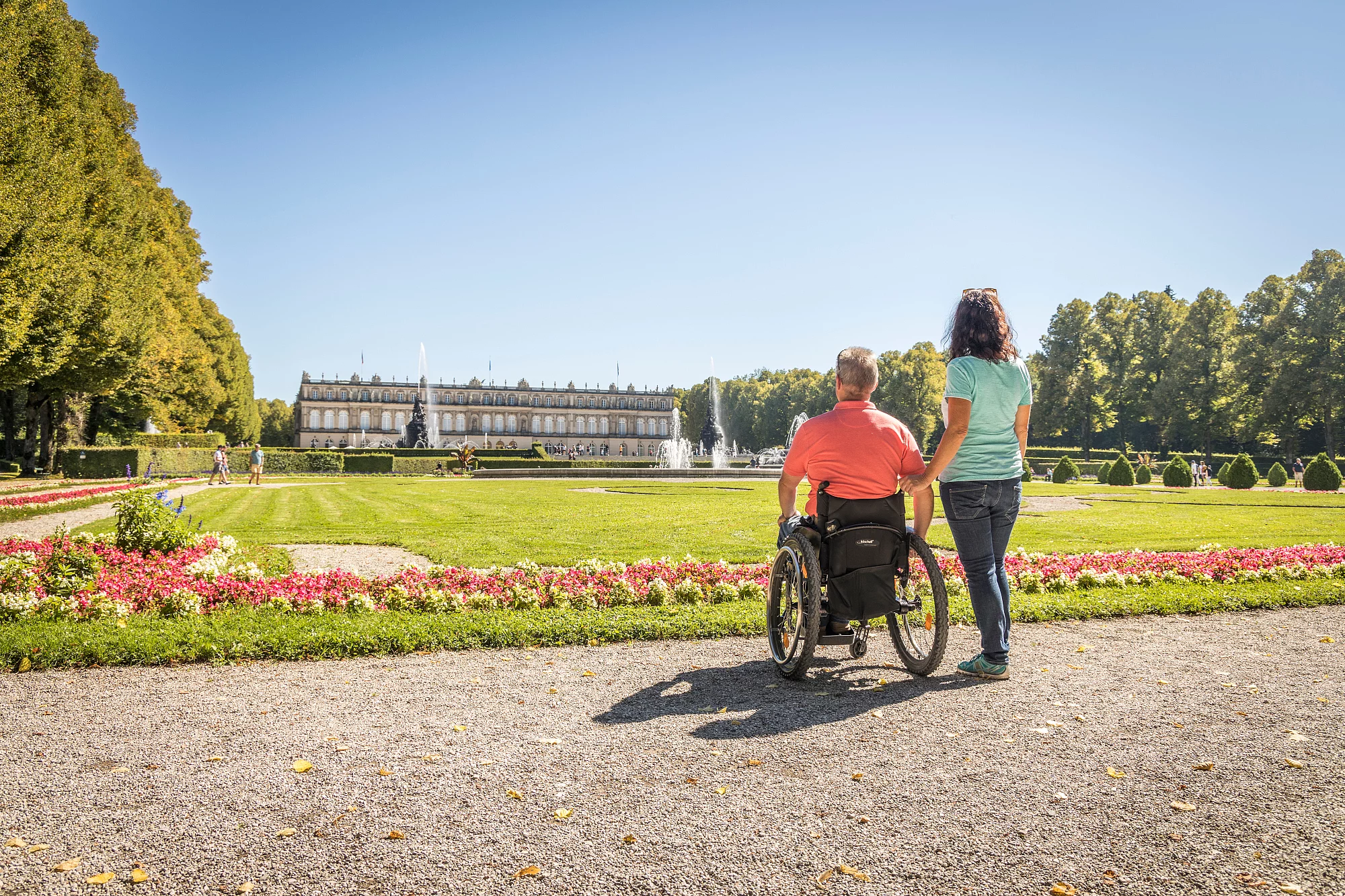 Schloss Herrenchiemsee mit Rollstuhlfahrer Rollstuhlfahrer vor der Kulisse von Schloss Herrenchiemsee