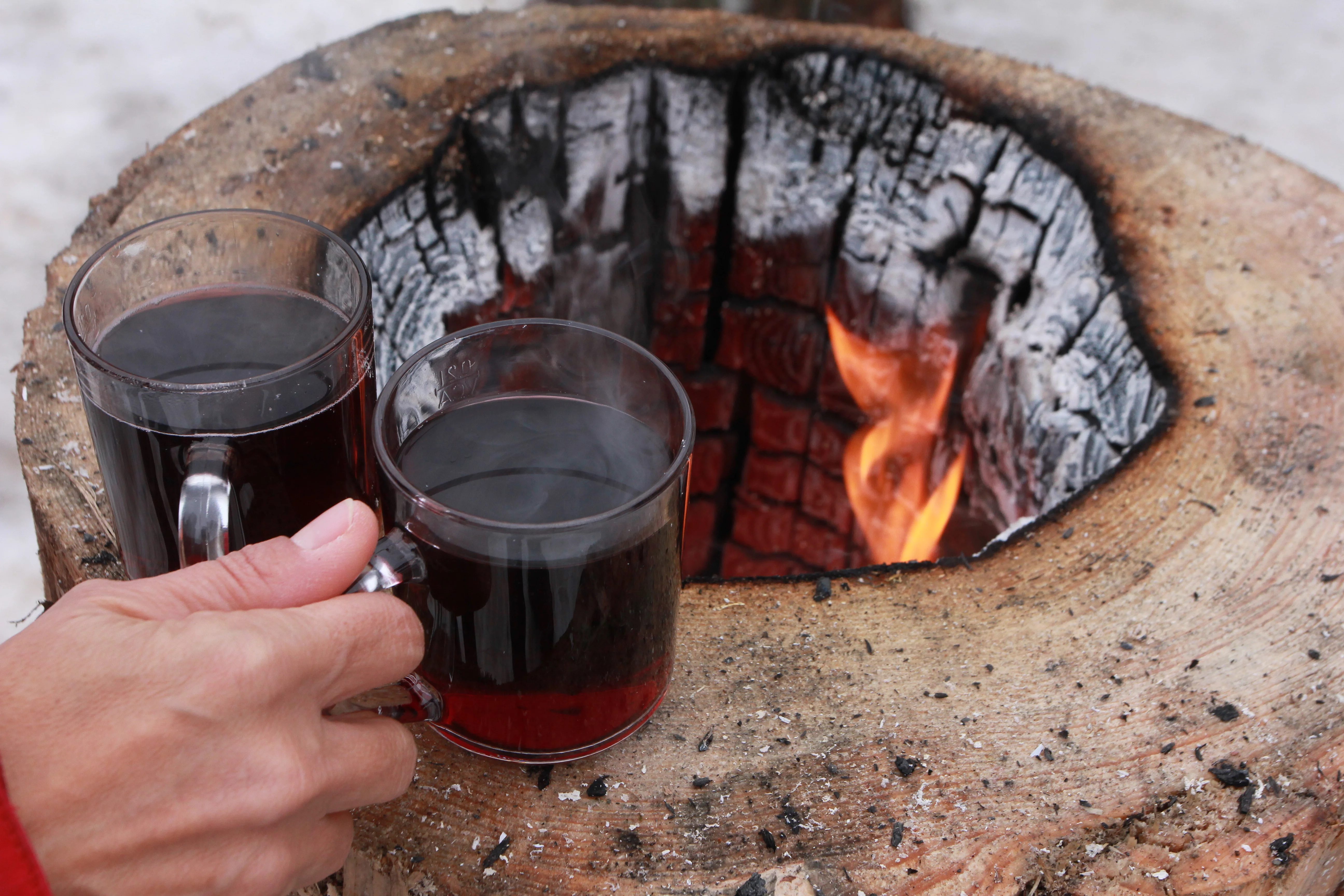 Eine Hand nimmt zwei Tassen Glühwein von einer offenen Feuerstelle
