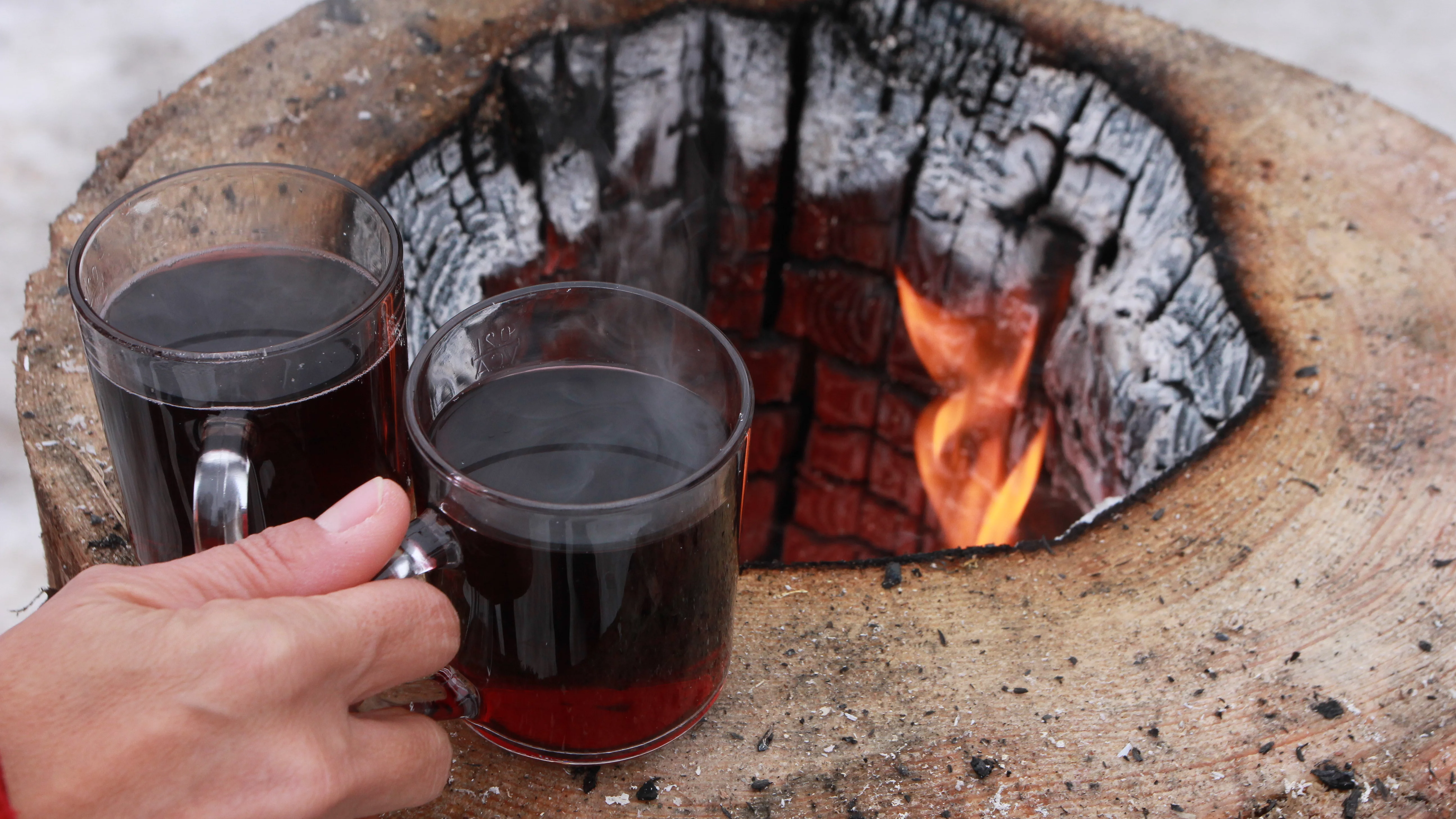 Eine Hand nimmt zwei Tassen Glühwein von einer offenen Feuerstelle