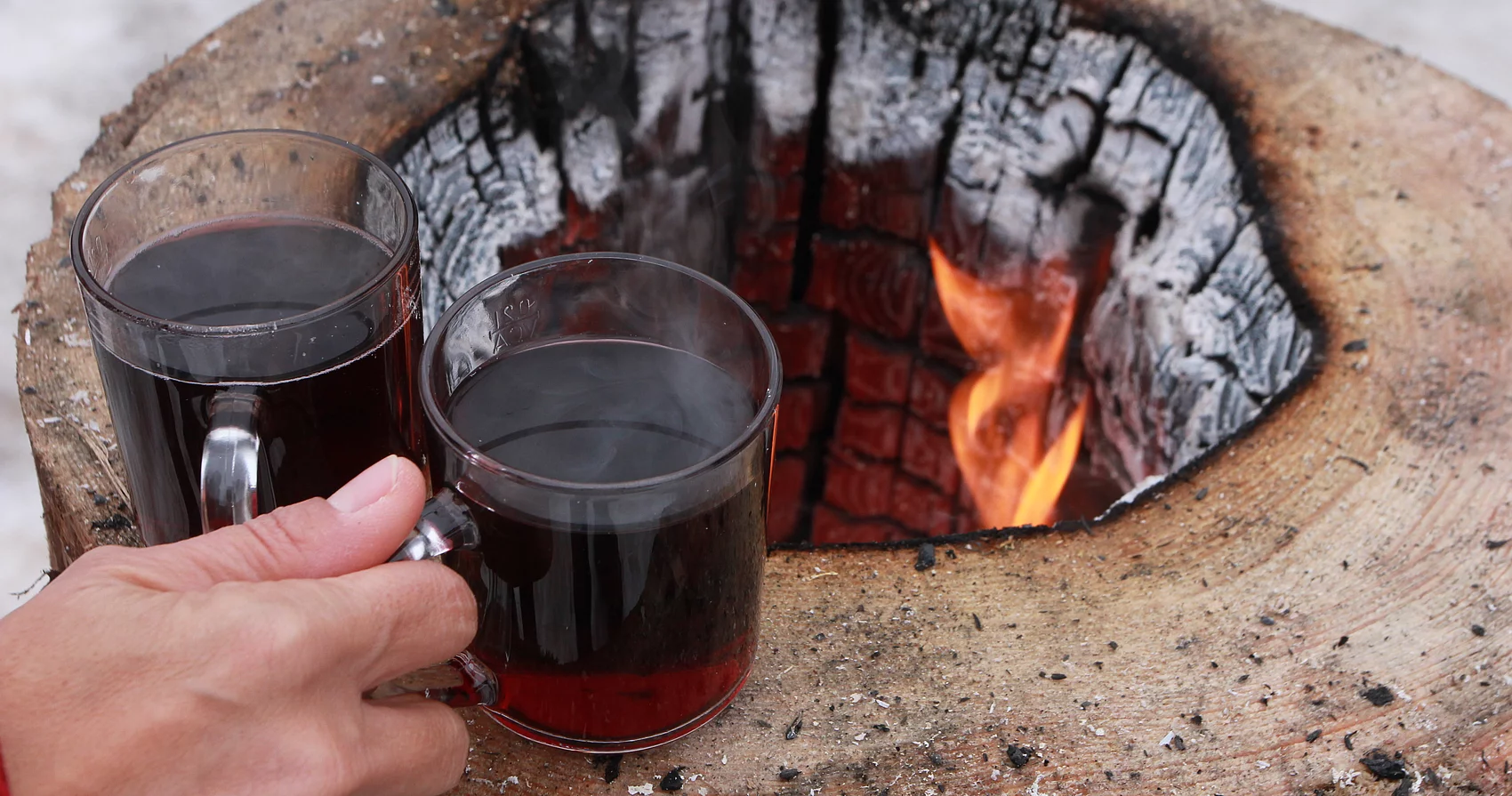 Eine Hand nimmt zwei Tassen Glühwein von einer offenen Feuerstelle