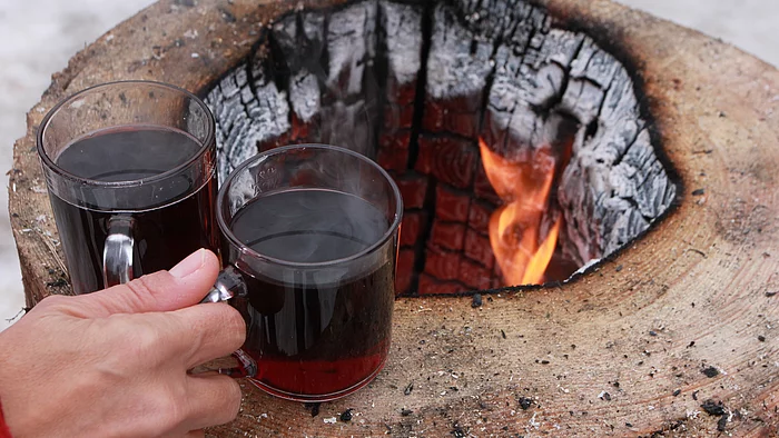 Eine Hand nimmt zwei Tassen Glühwein von einer offenen Feuerstelle